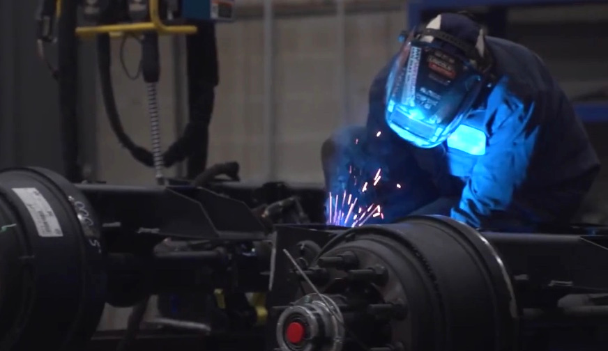 Welder joining an industrial component beside heavy equipment