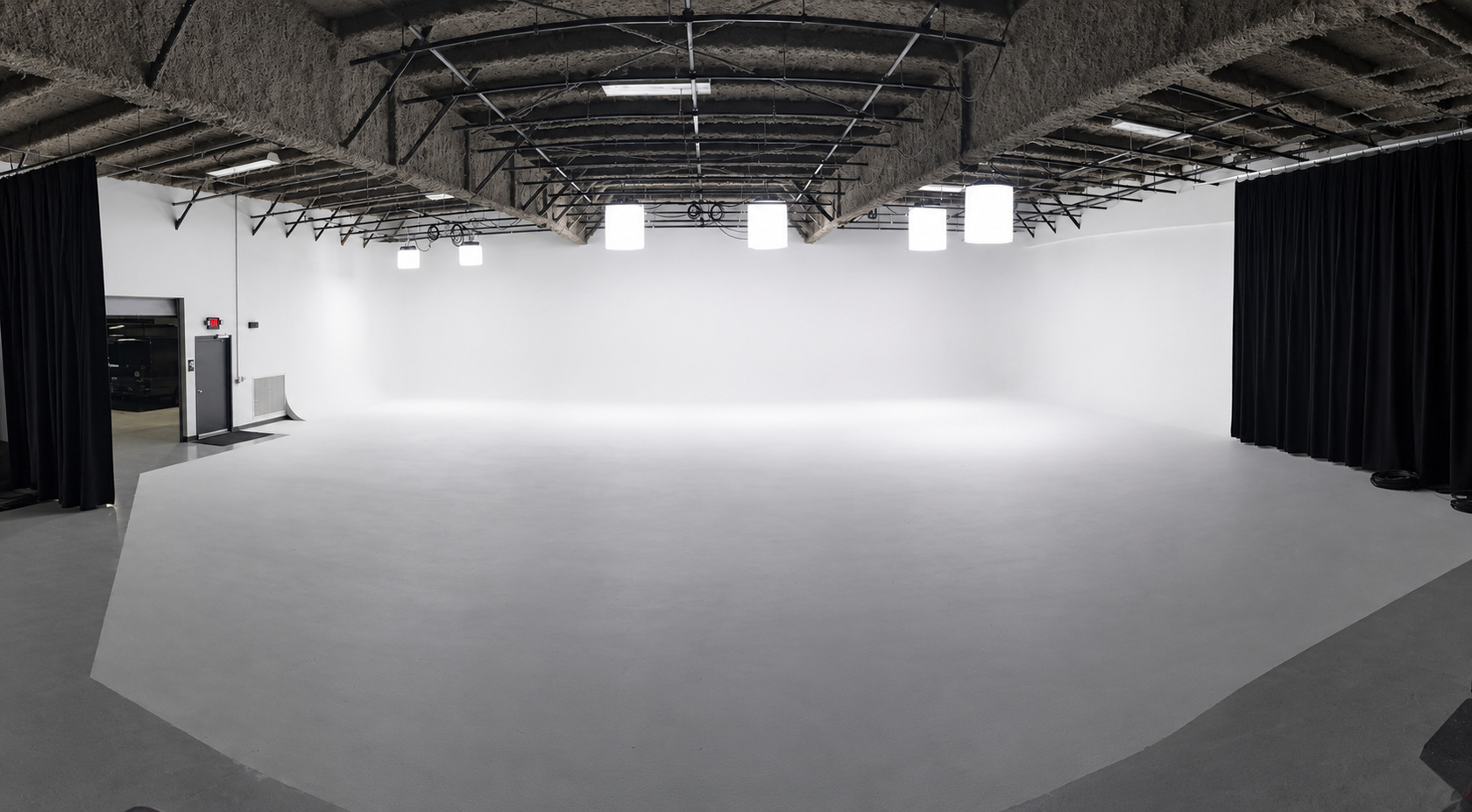 Empty white studio with a curved backdrop, overhead lights, and black curtains