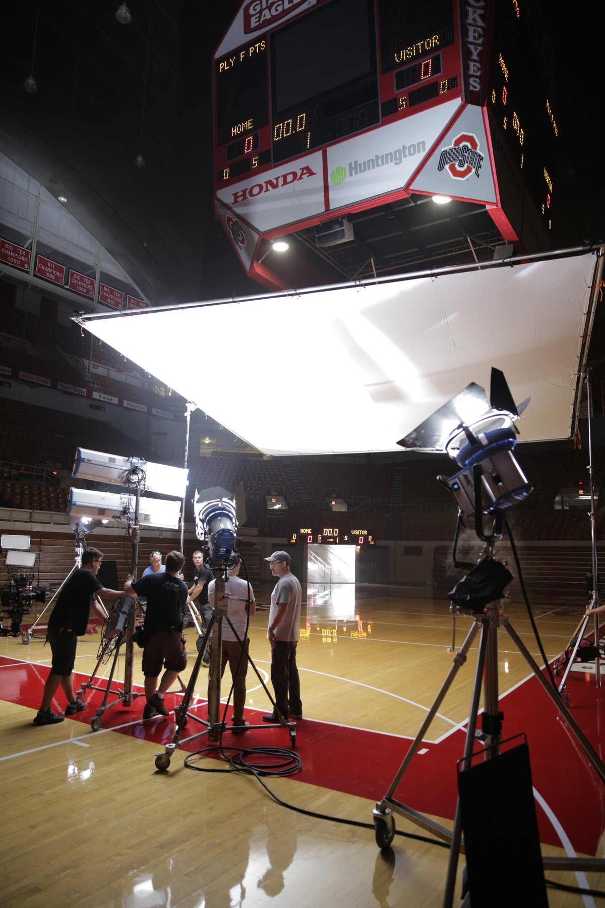 Crew preparing large lights and overhead diffusion on a basketball court