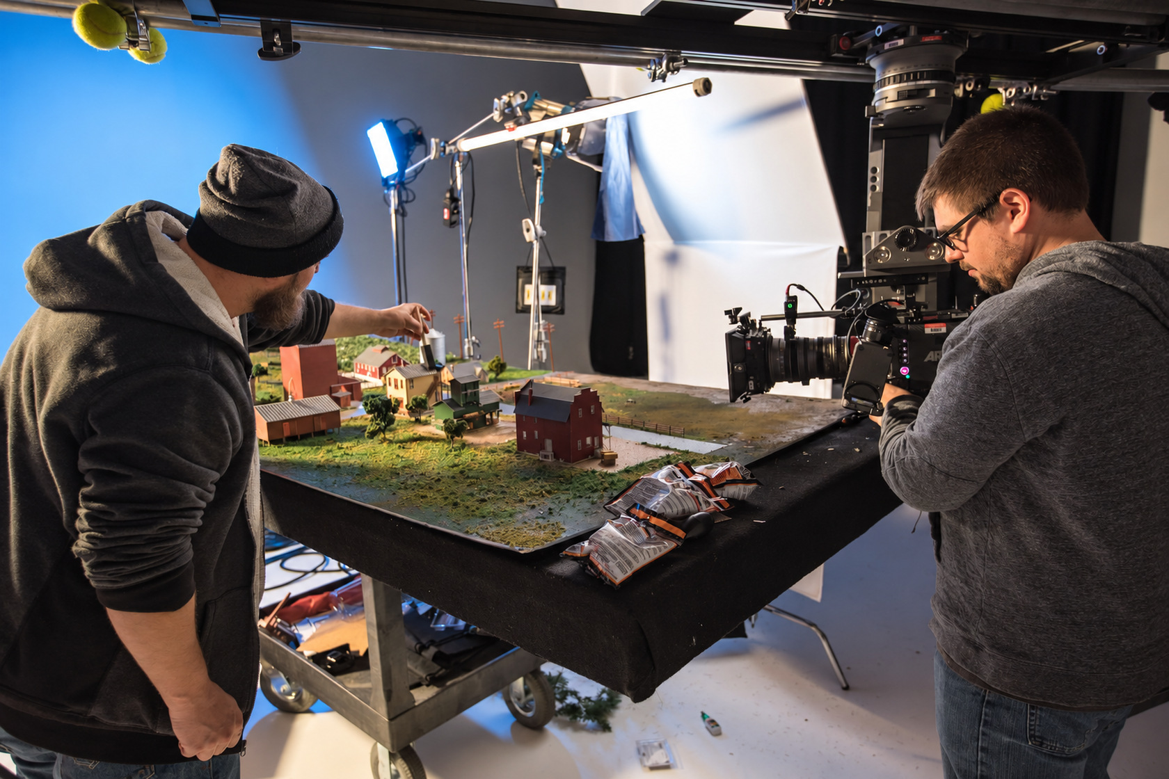 Two crew members preparing a miniature farm set and a cinema camera