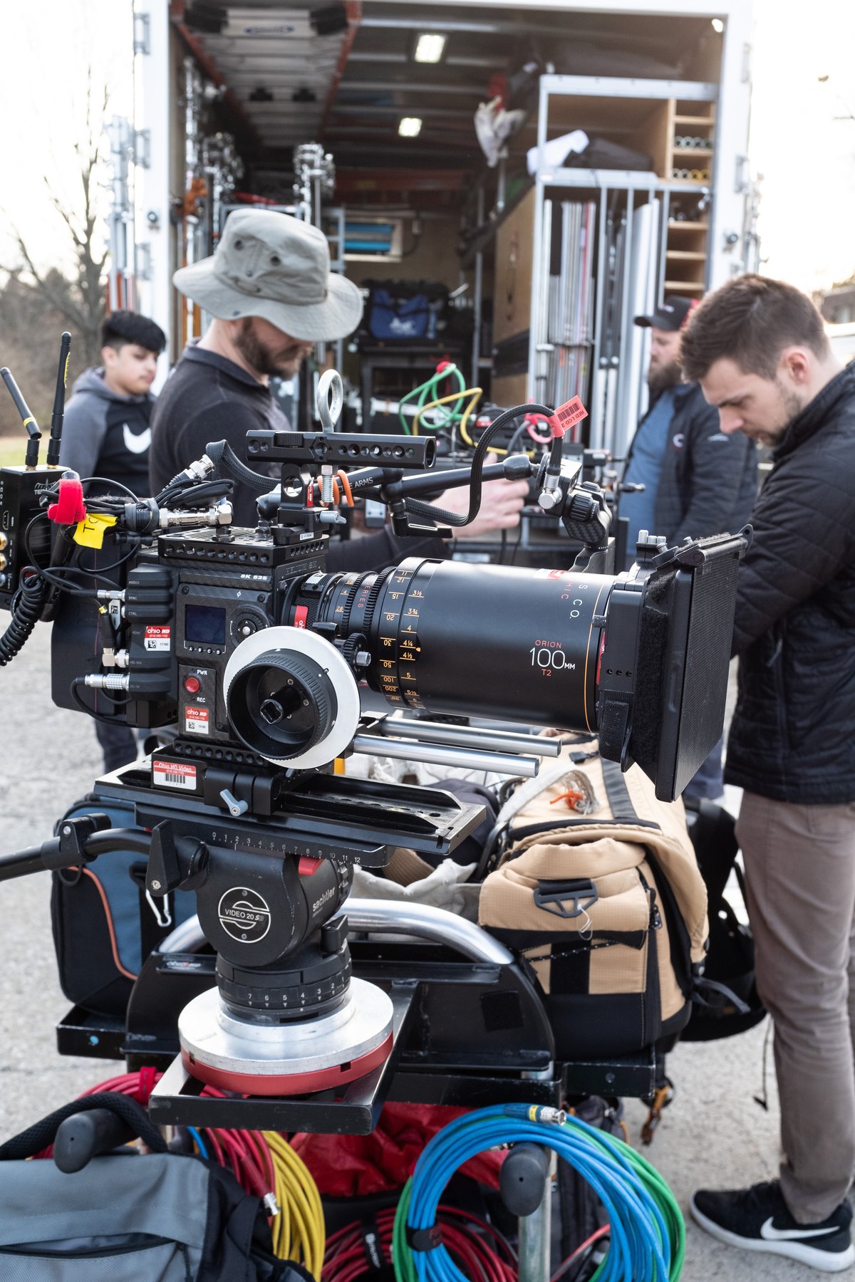 Cinema camera on a cart with crew preparing equipment beside a loaded truck