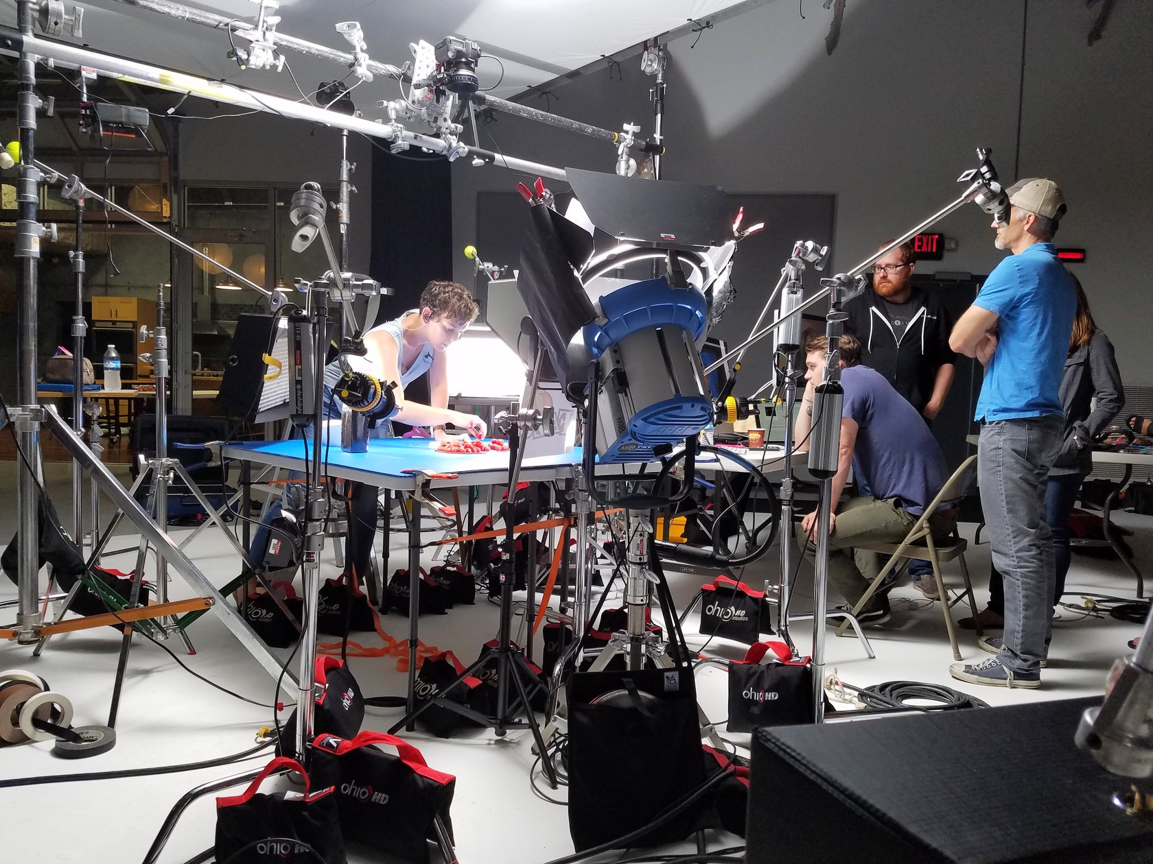 Crew preparing a tabletop food scene with overhead cameras and film lighting