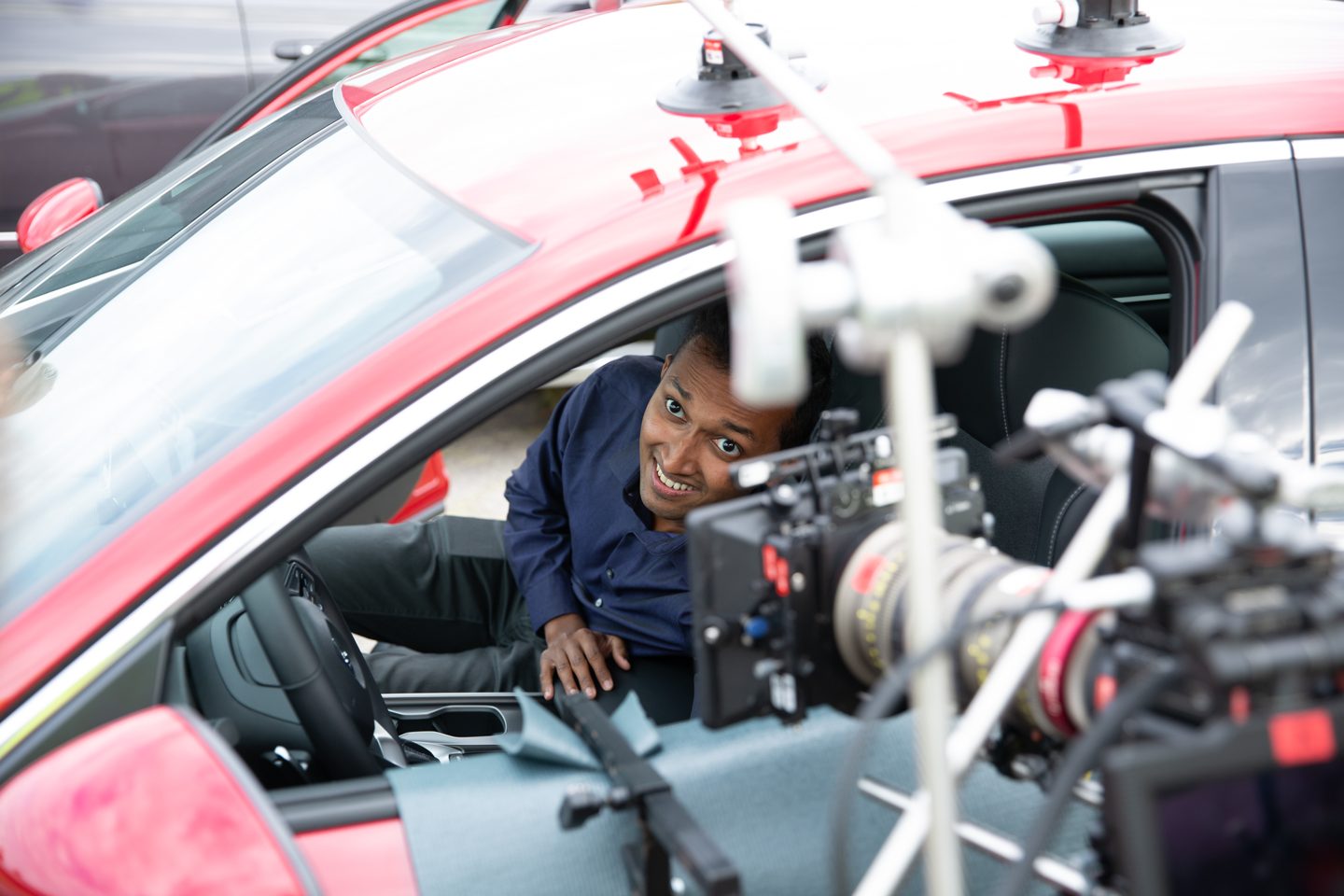 Crew preparing a camera rig at the window of a red Honda