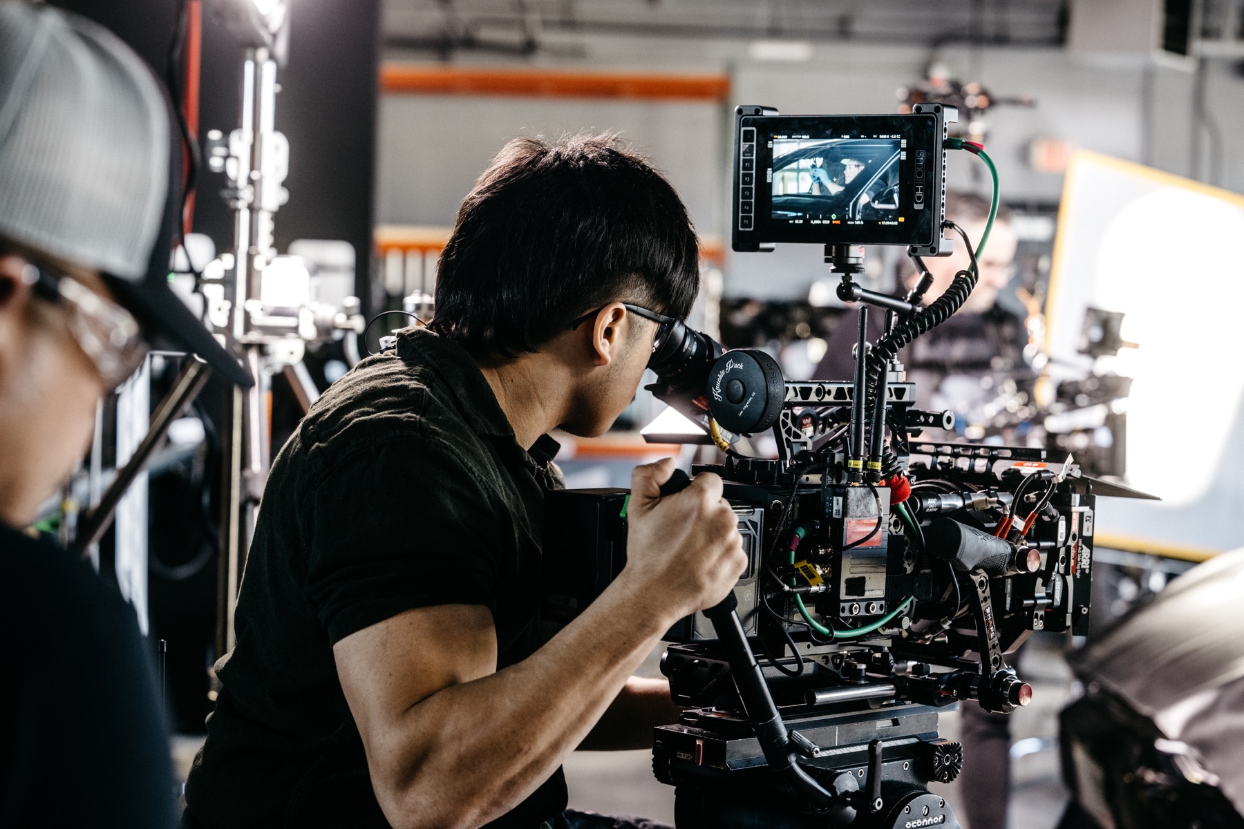 Camera operator framing a windshield shot, with the vehicle visible on the camera monitor
