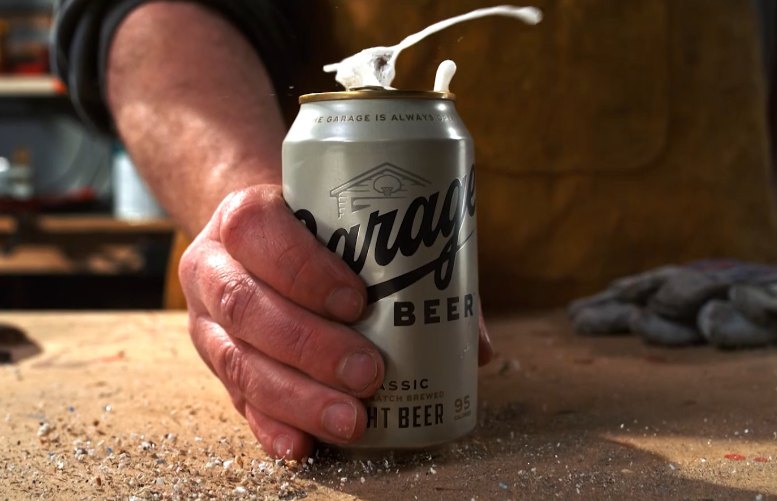 Foam splashing above a beer can held on a workbench