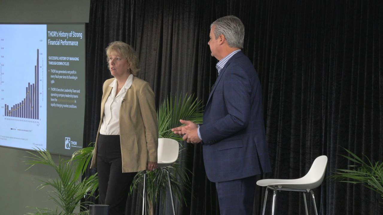 Two presenters on stage beside a presentation screen at THOR Investor Day