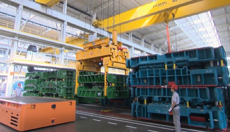 Wide view of a Demag crane moving industrial tooling across a factory floor